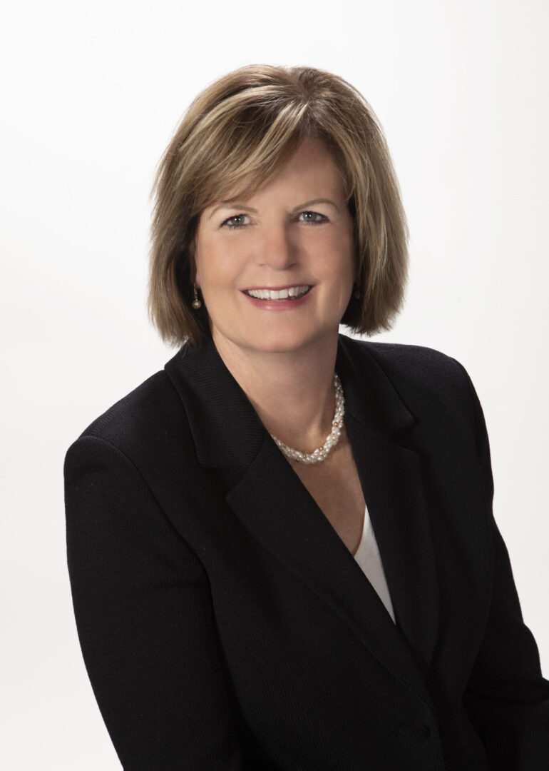 A woman in black jacket and white shirt smiling.